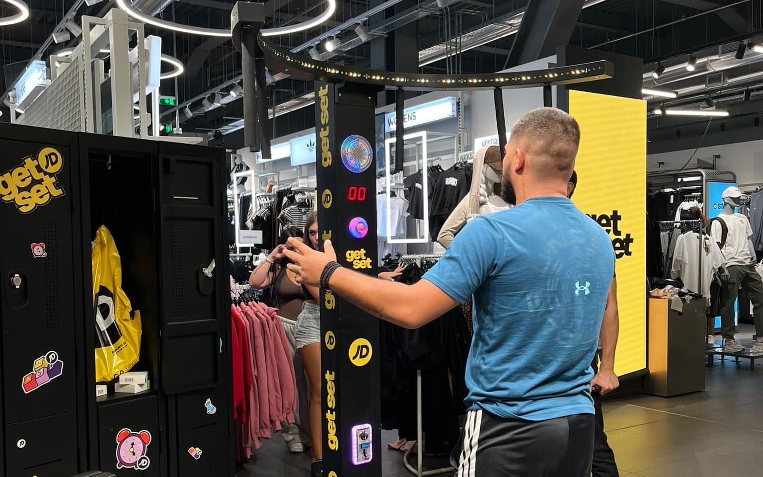 A shopper reaching for the buttons on the JD branded Falling Sticks column inside a JD Sports store